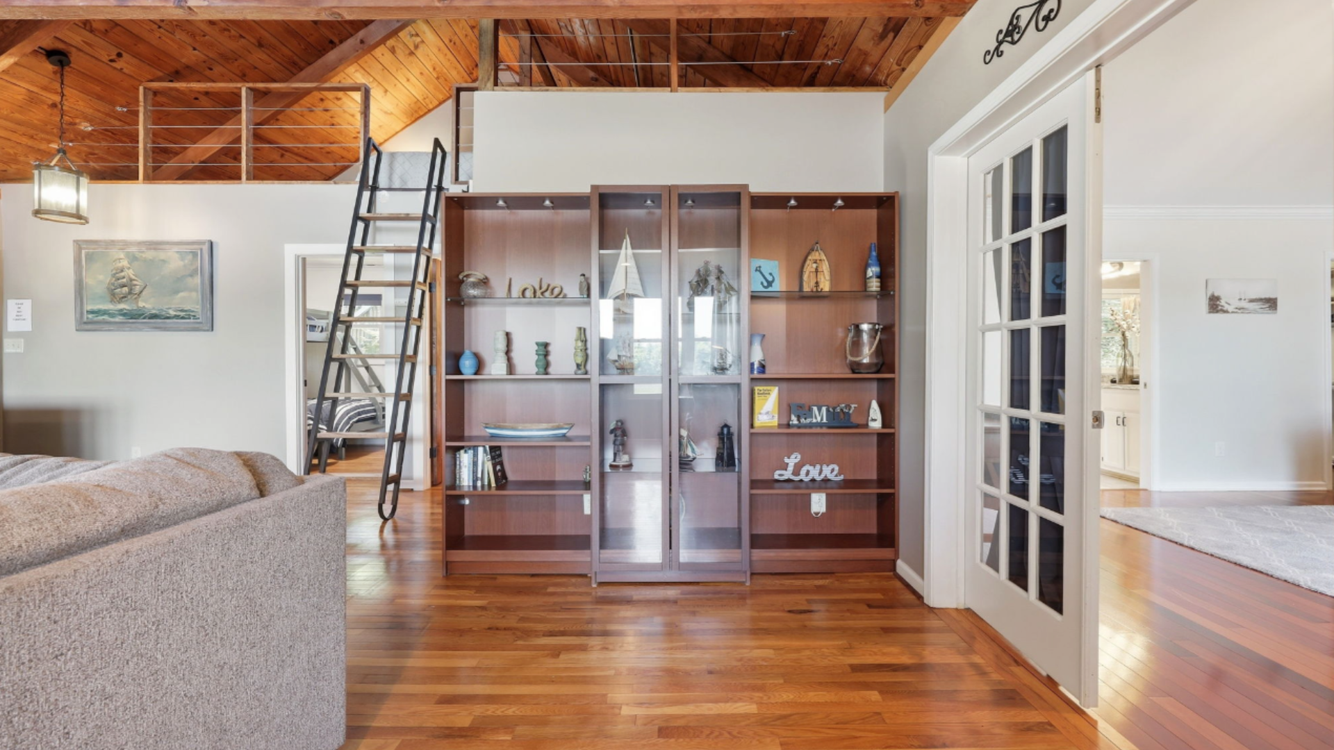Living room with wood floors, loft ladder, glass cabinet, and French doors under a sloped wooden ceiling