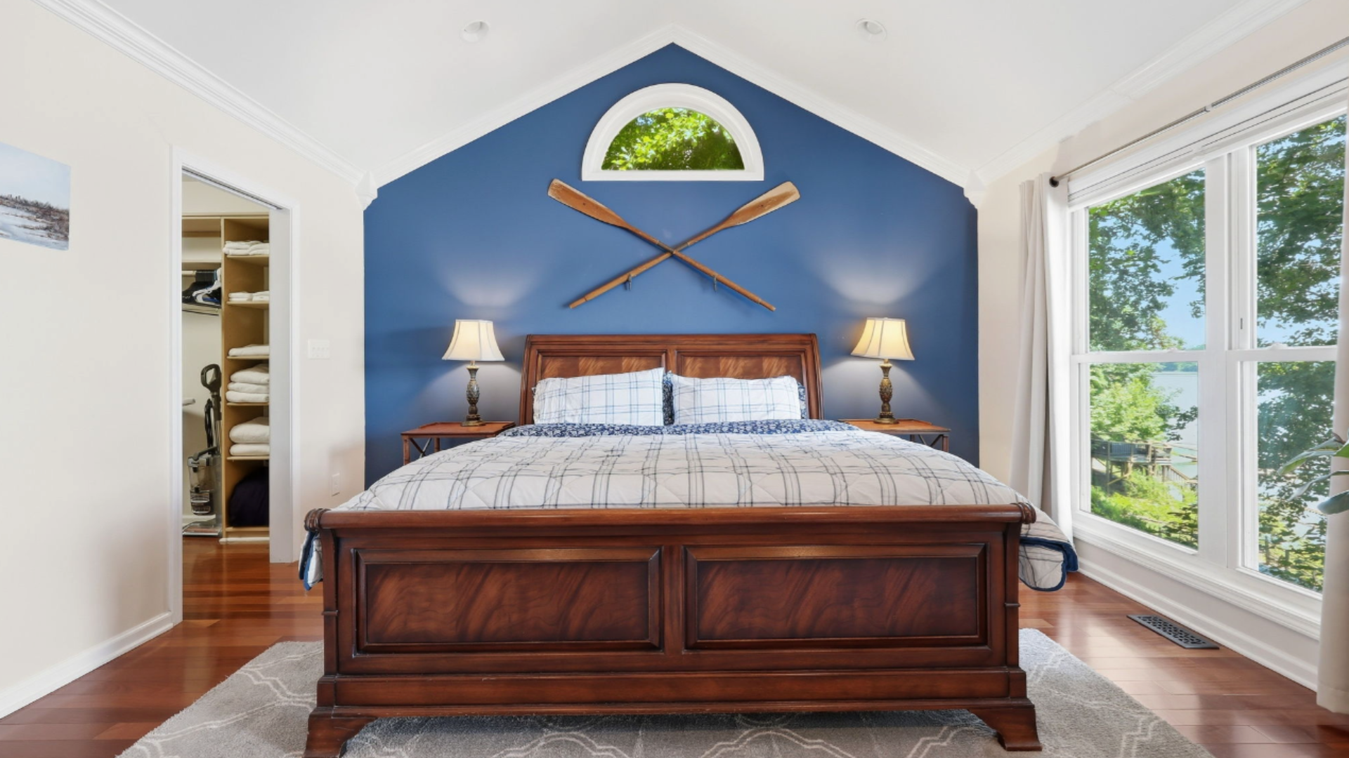 Bright blue bedroom with wooden bed, vaulted ceiling, bedside lamps, and large windows.