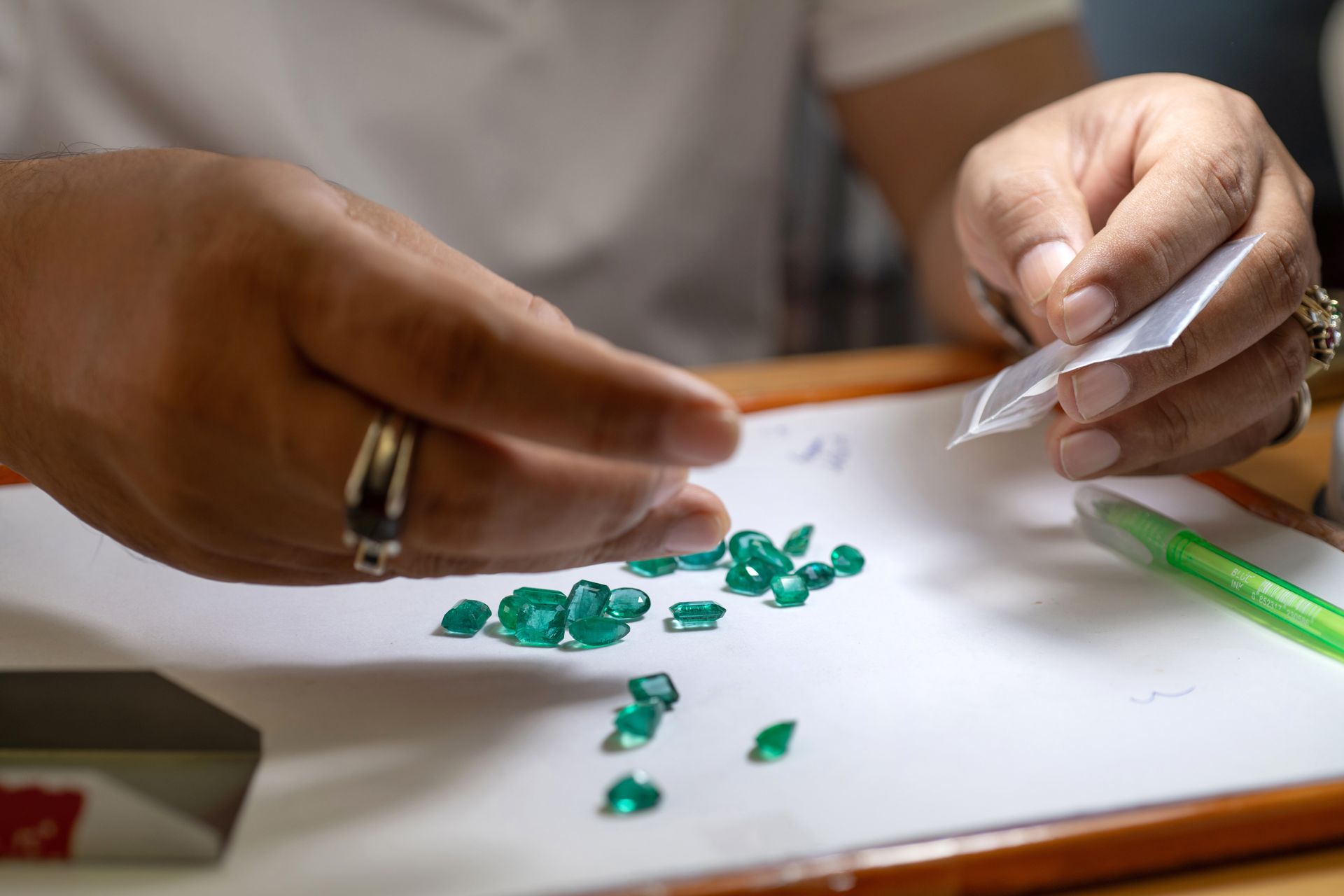 A close-up of a buyer carefully appraising emeralds on a piece of paper while holding a plastic bag.