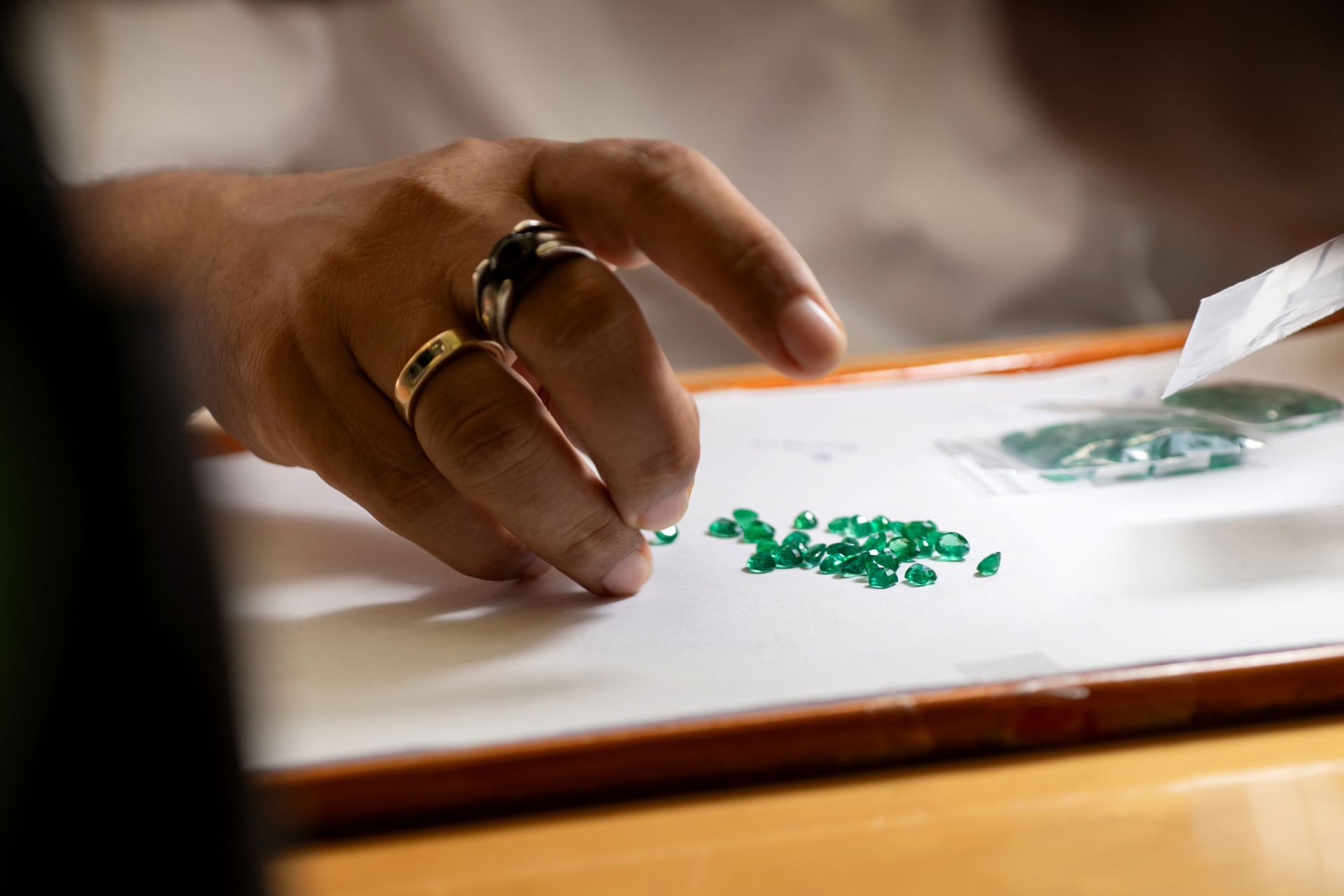 Close-up of a buyer examining emeralds on paper while holding a plastic bag.
