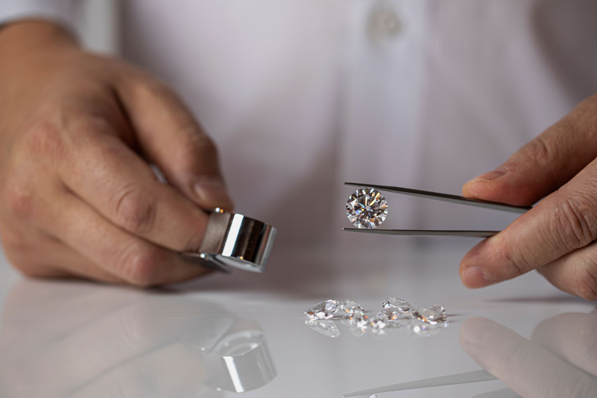 A close-up of a jeweler holding a diamond with forceps and a loupe with the other hand. A close-up of a jeweler holding a diamond with forceps and a loupe with the other hand.
