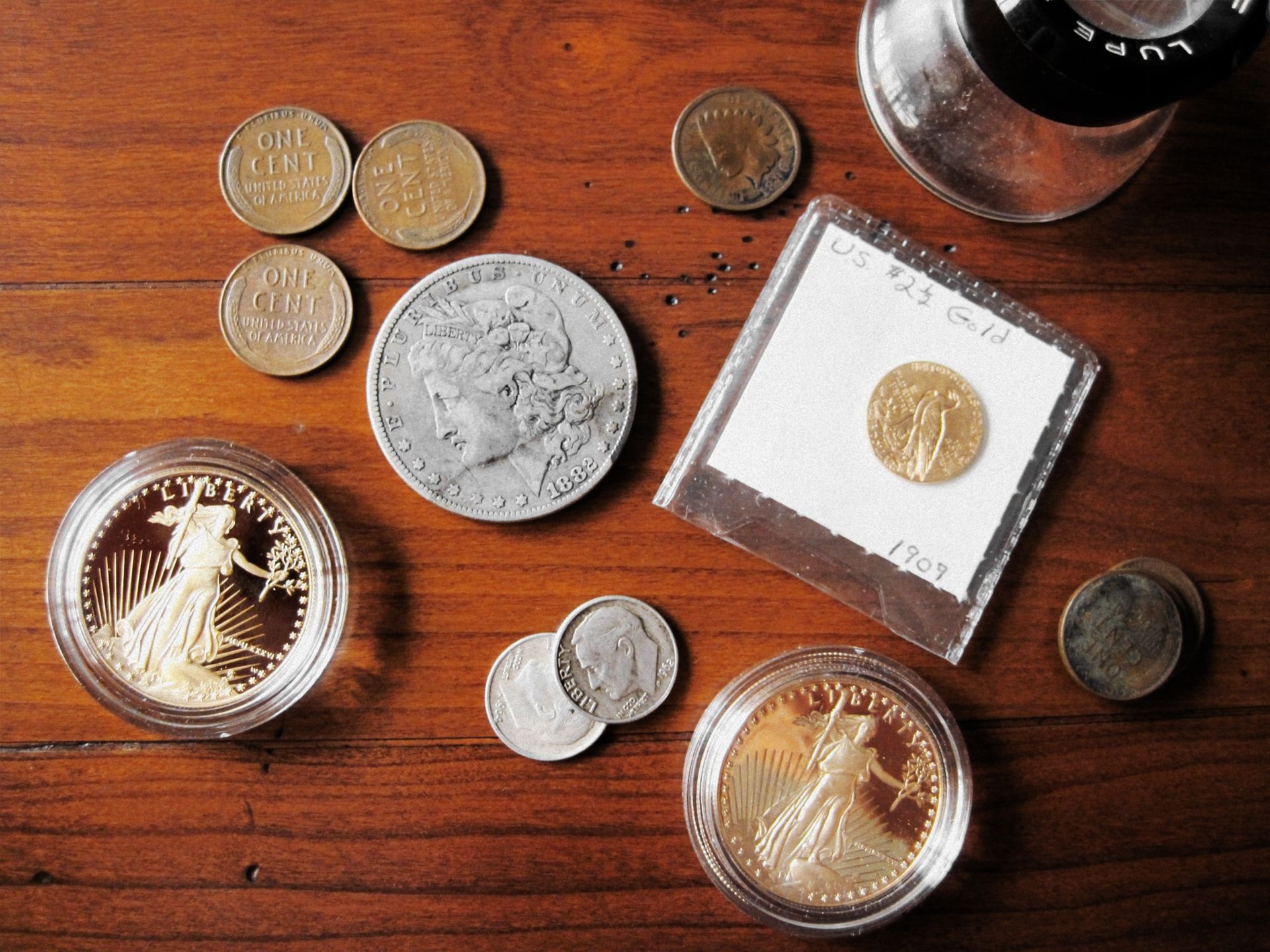 Assorted coins on a wooden surface, including gold, silver, and copper. Some coins are in protective cases.