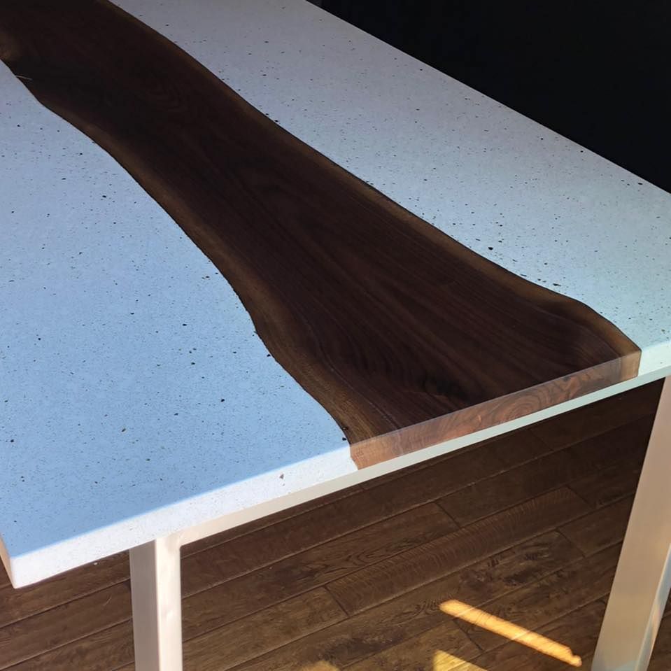 Une table moderne composée d'un plateau en bois foncé aux bords naturels, centré entre deux panneaux de béton moucheté gris clair.