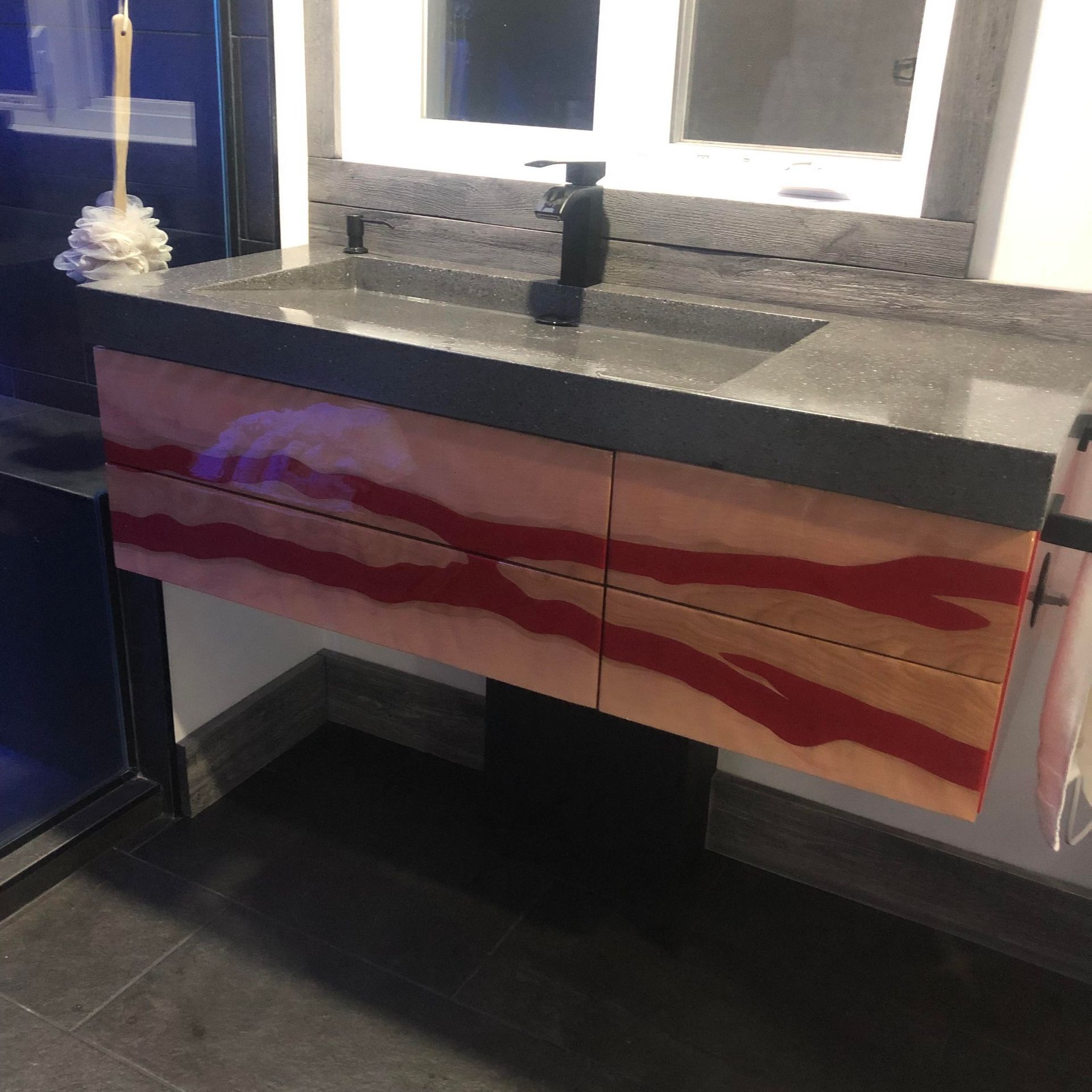 Un meuble-lavabo mural avec un lavabo en pierre grise et des tiroirs d'armoire ornés d'un motif rouge et beige rappelant le bacon.