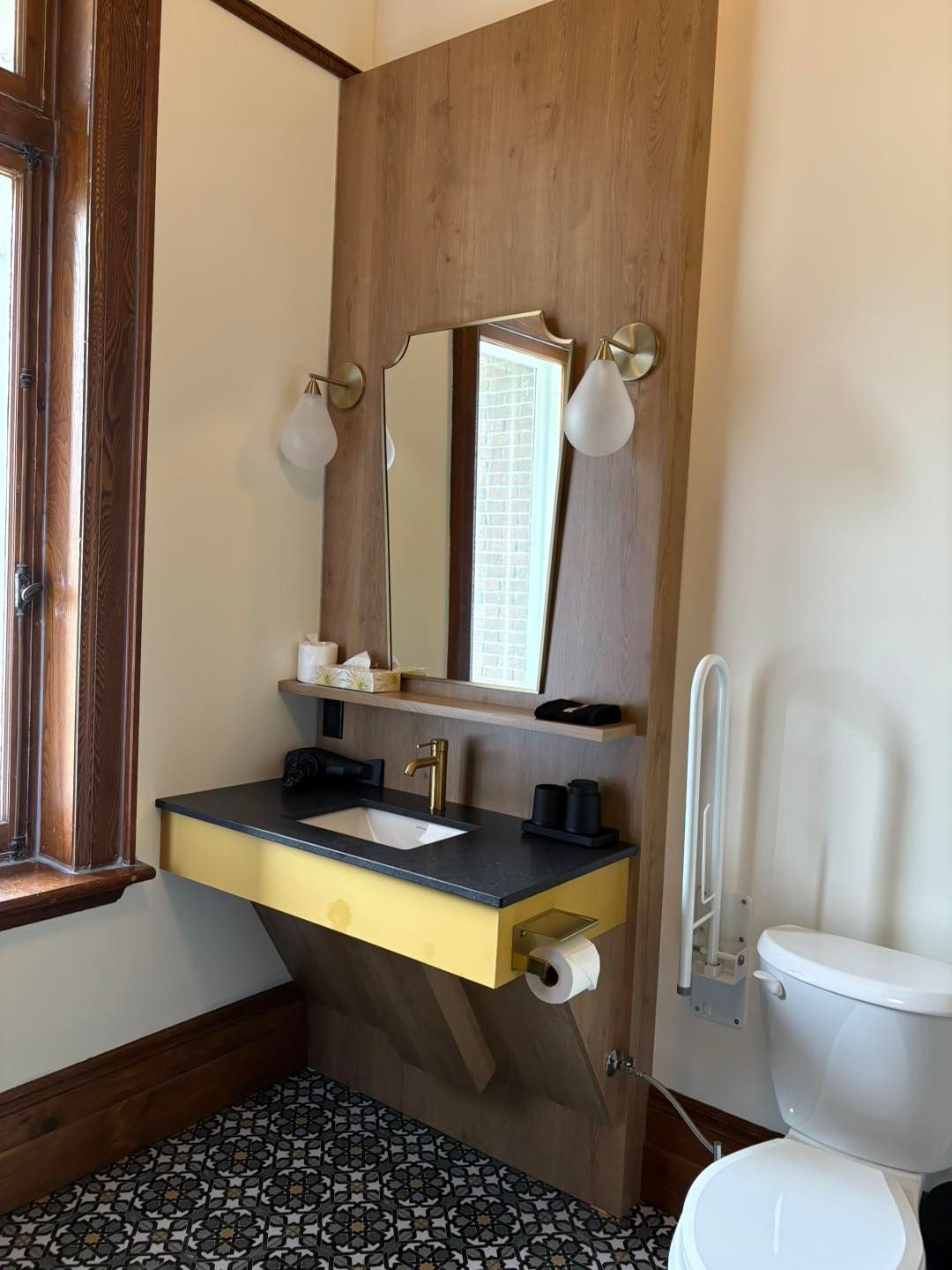 Un meuble-lavabo avec une base jaune, un plan de travail foncé et un mur lambrissé, comprenant un miroir, des luminaires et des toilettes.