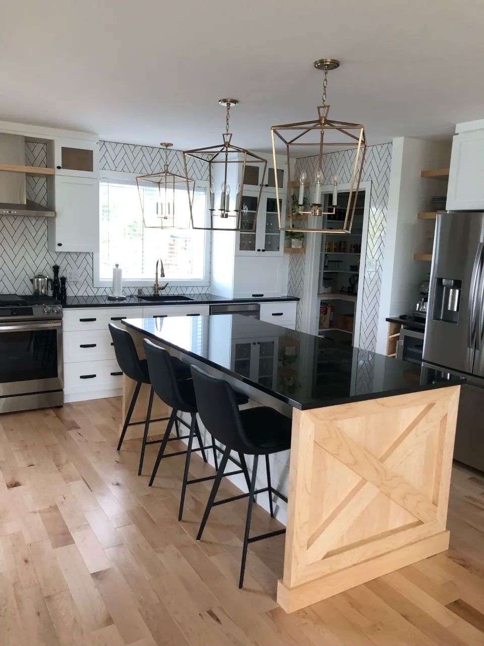 Cuisine moderne avec un îlot noir, trois tabourets de bar noirs, un parquet clair, des placards blancs et deux lanternes dorées.