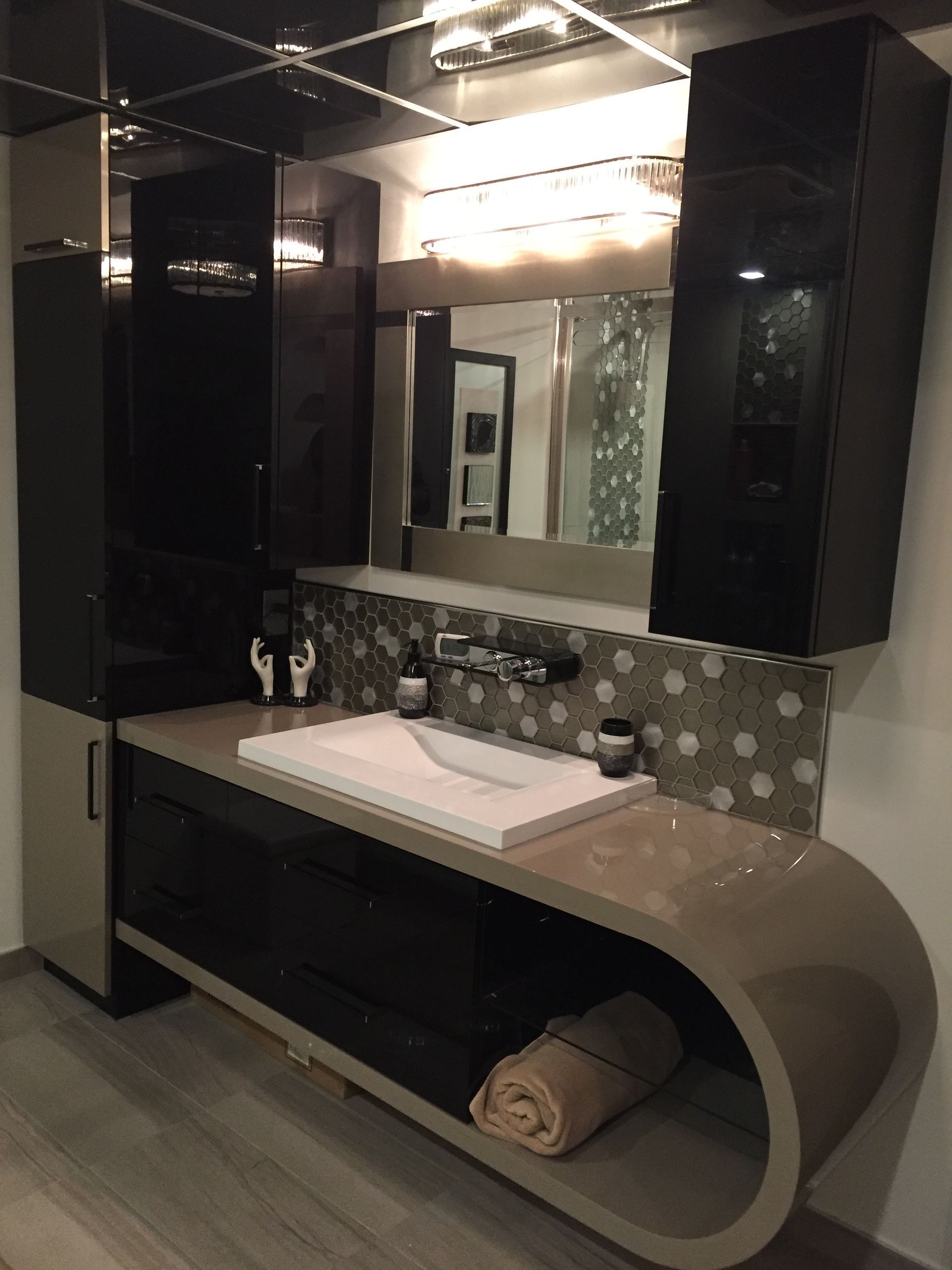 Meuble-lavabo moderne avec armoires noires, comptoir beige incurvé, lavabo blanc et crédence en mosaïque.