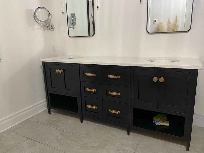 Meuble-lavabo double noir avec robinetterie dorée, comptoir en marbre blanc et deux miroirs contre un mur blanc.