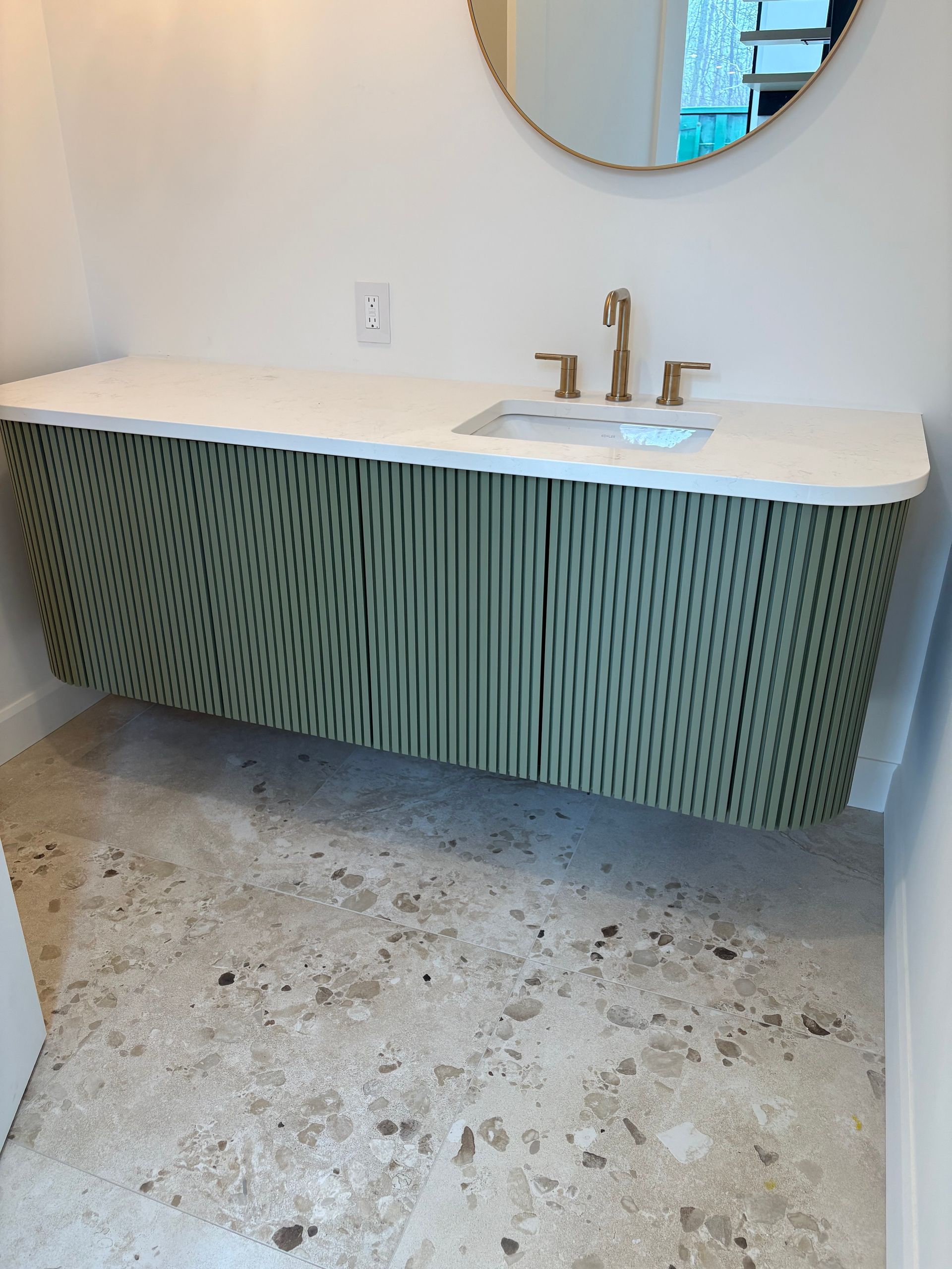 Un meuble-lavabo suspendu avec une finition texturée à rayures vertes, un comptoir blanc, un robinet doré et un sol en carrelage de pierre.