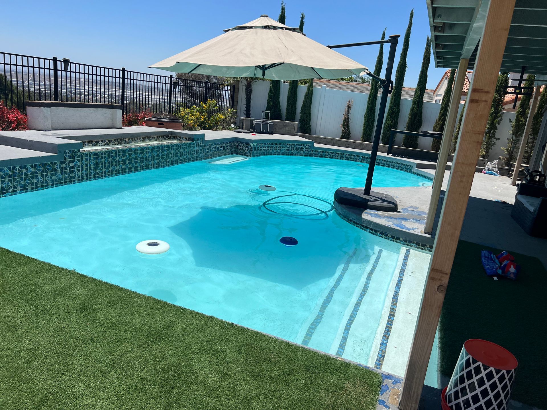 A pool with turquoise water, a beige umbrella, and a green lawn on a sunny day.