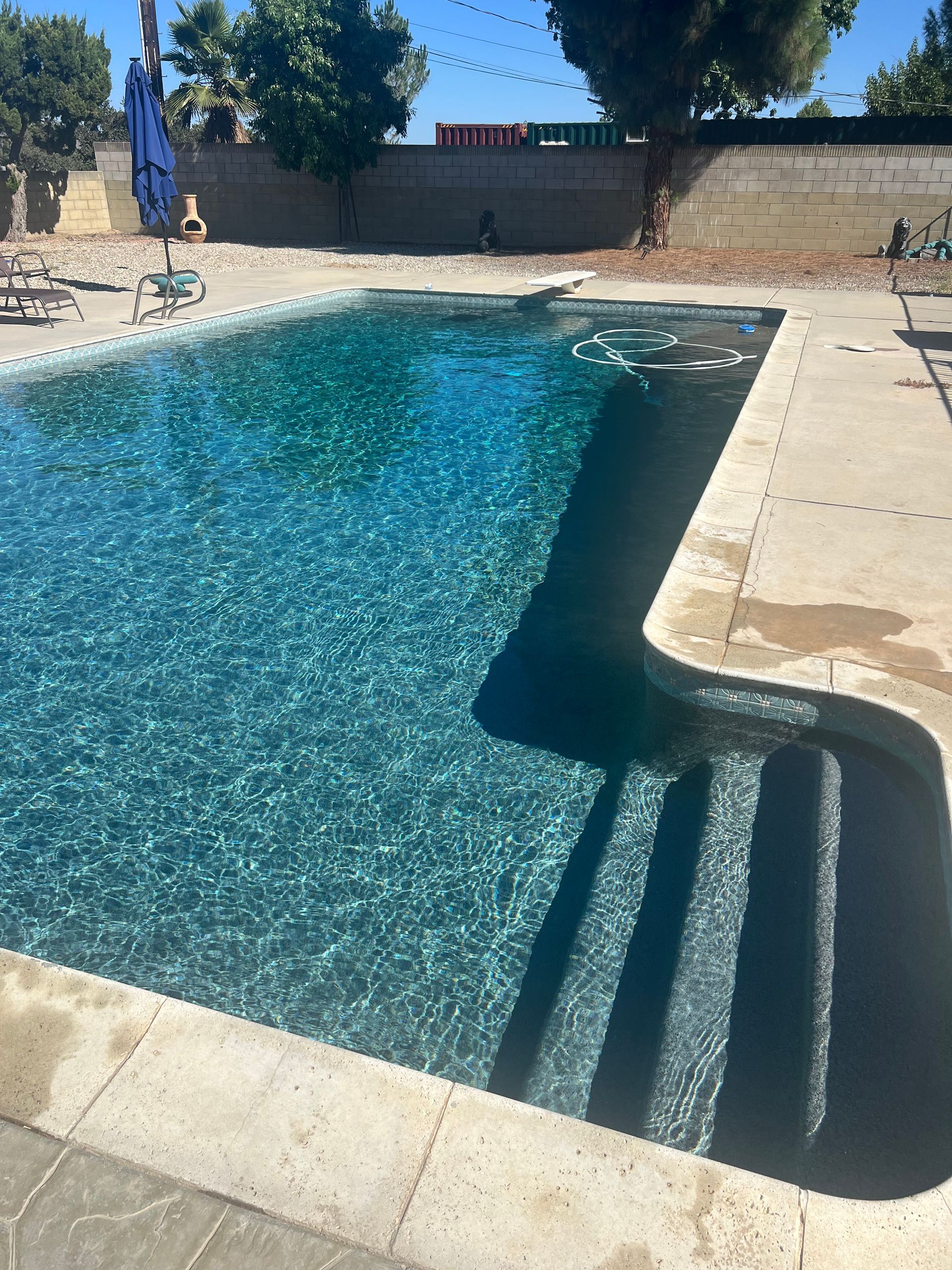 Swimming pool with steps. Turquoise water, concrete deck, blue sky, and a fence.