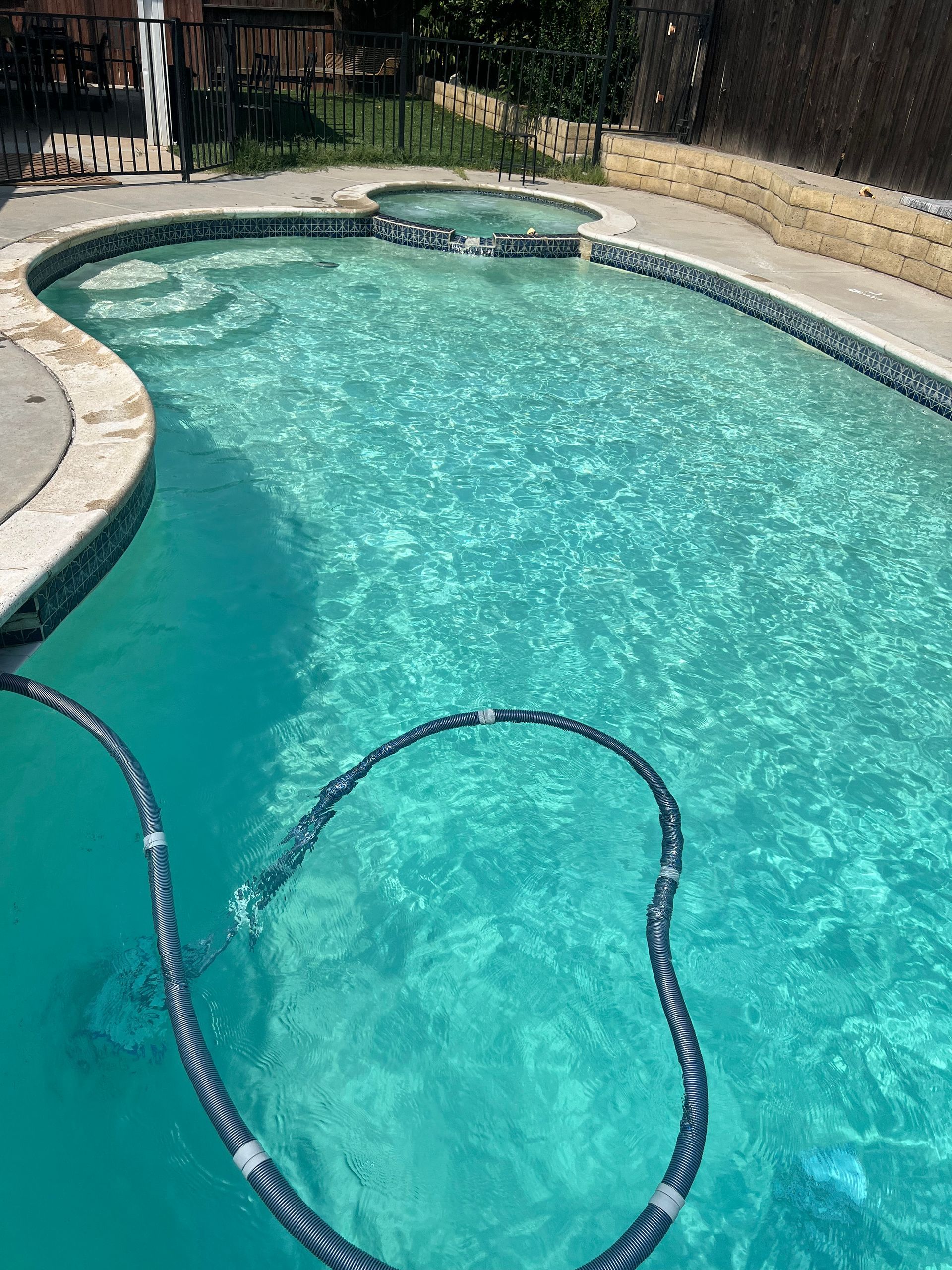 Swimming pool with turquoise water, a hose, and a hot tub.