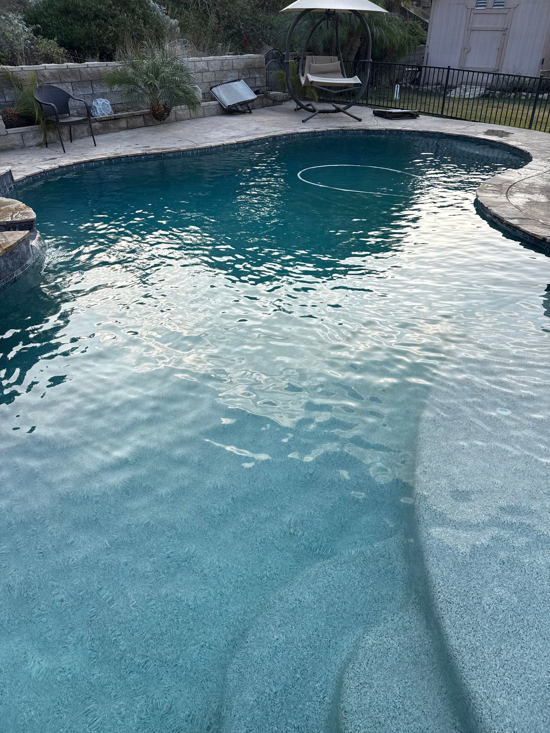 Pool of clear, blue water with a stone border and a patio umbrella in the background.