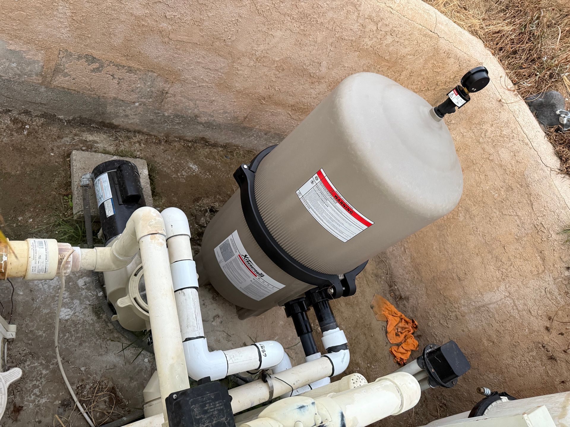 Swimming pool equipment: gray filter tank and white pipes in a concrete utility pit.
