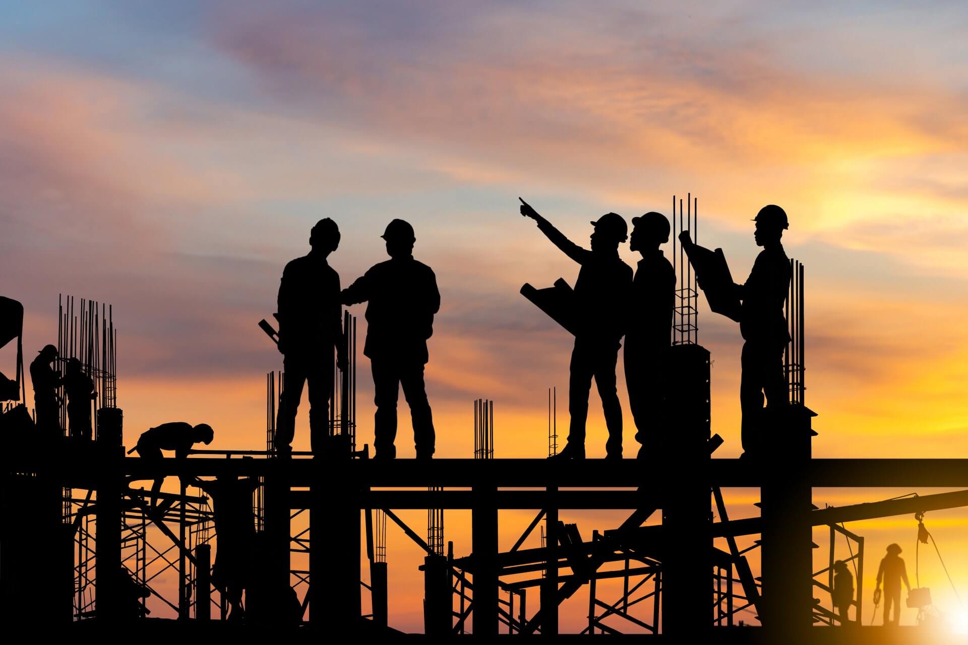 A group of construction workers are working on a construction site at sunset.