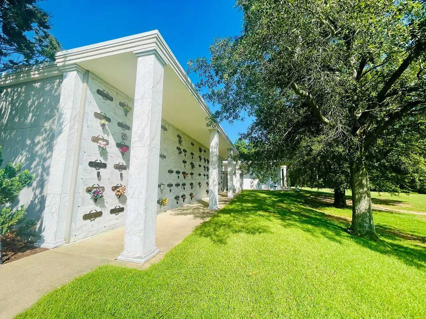 White building with columns beside a grassy lawn and trees under a bright blue sky