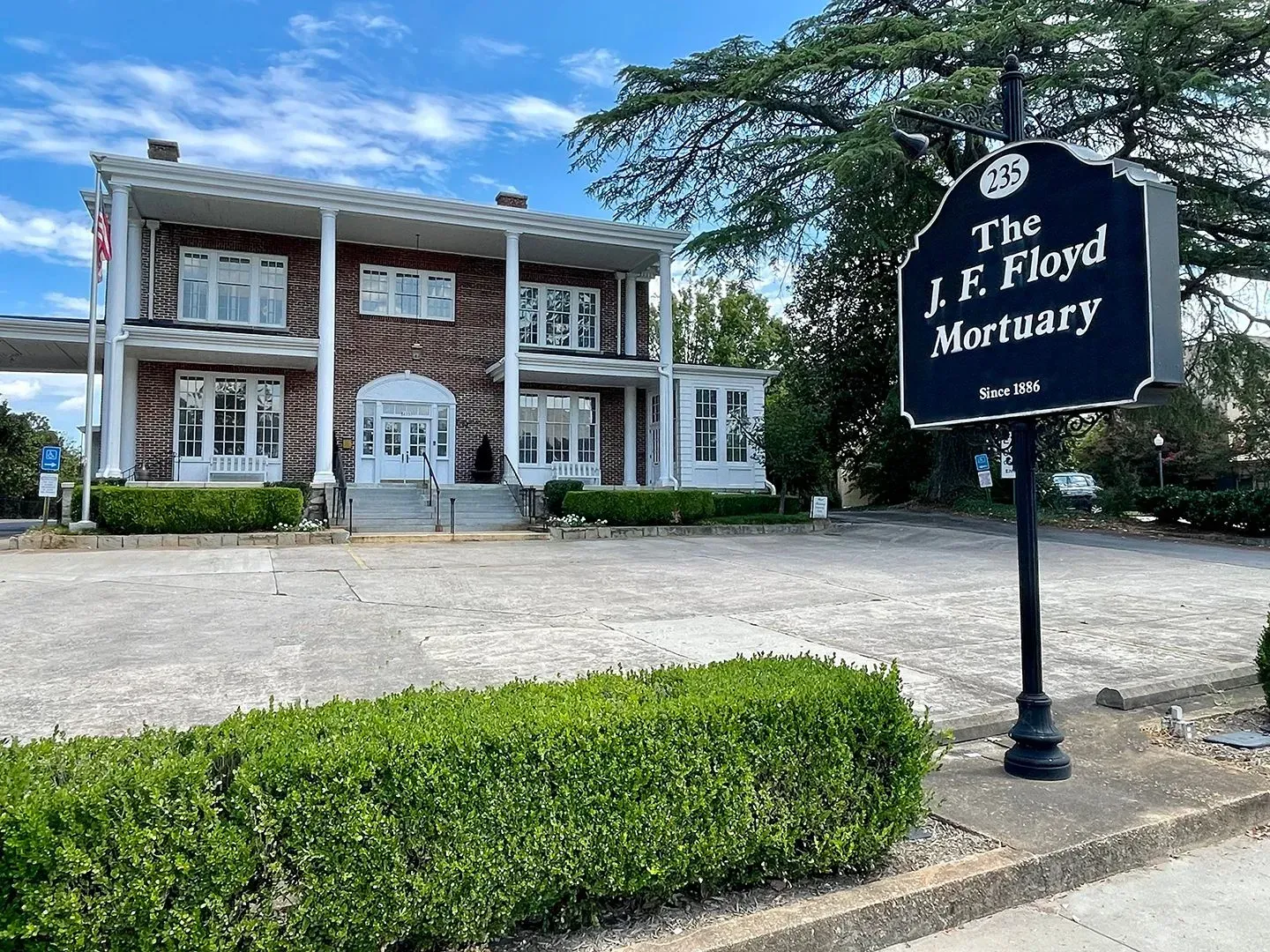 The J.F. Floyd Mortuary building with a sign and manicured hedge under a blue sky