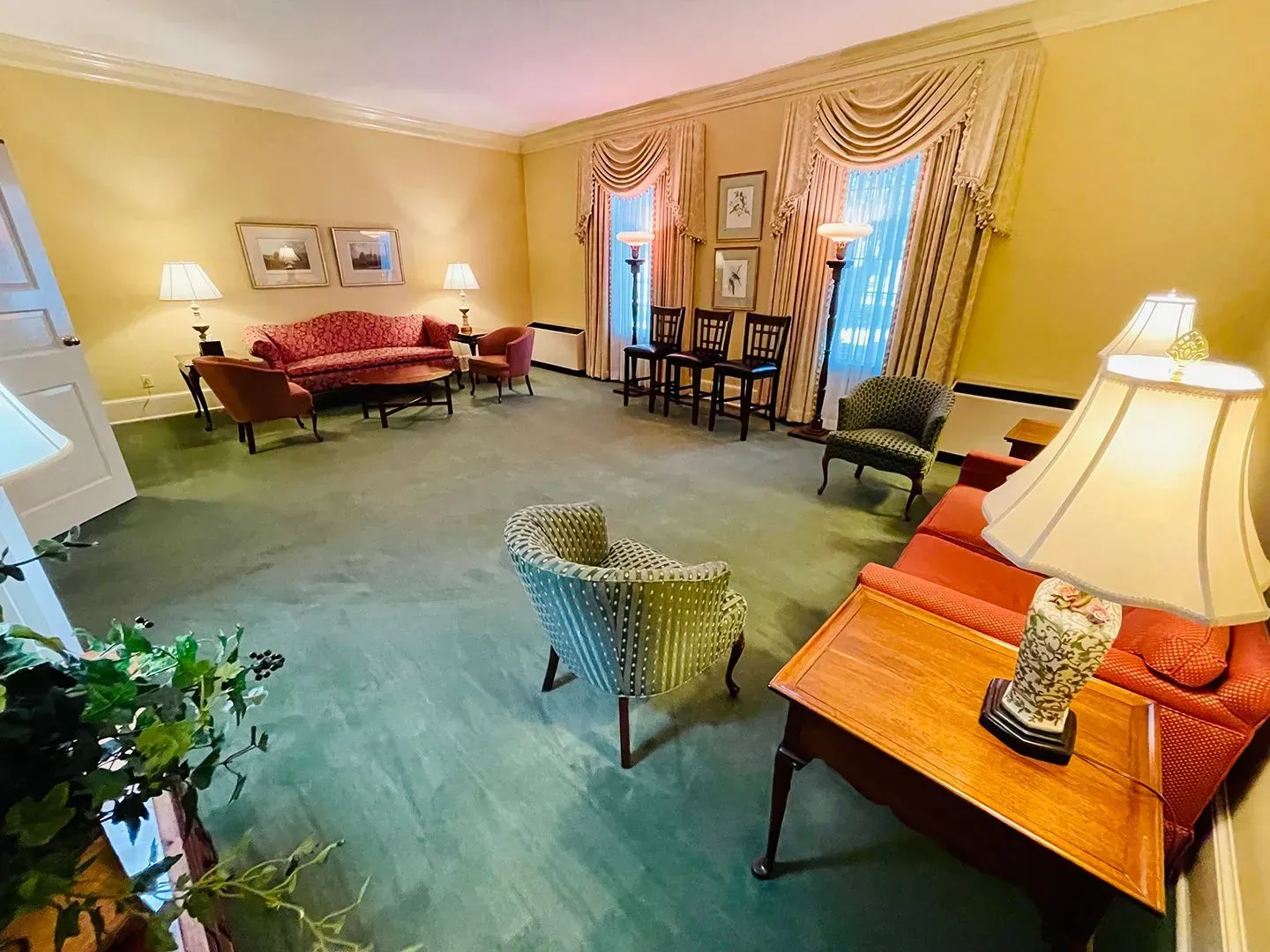 Elegant yellow sitting room with red sofas, green carpet, and tall curtained windows