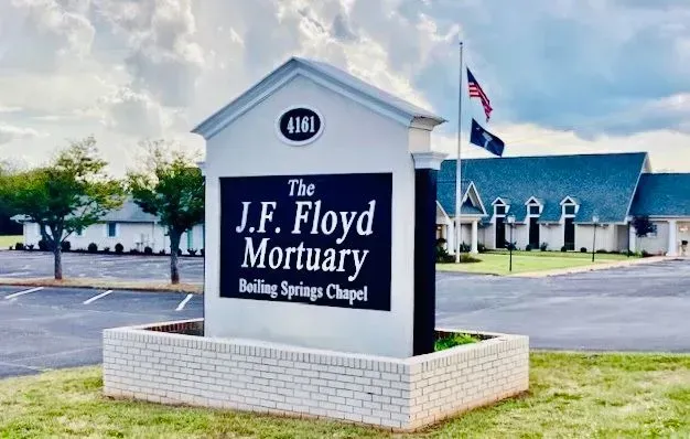 J.F. Floyd Mortuary sign outside a white brick funeral home under a partly cloudy sky