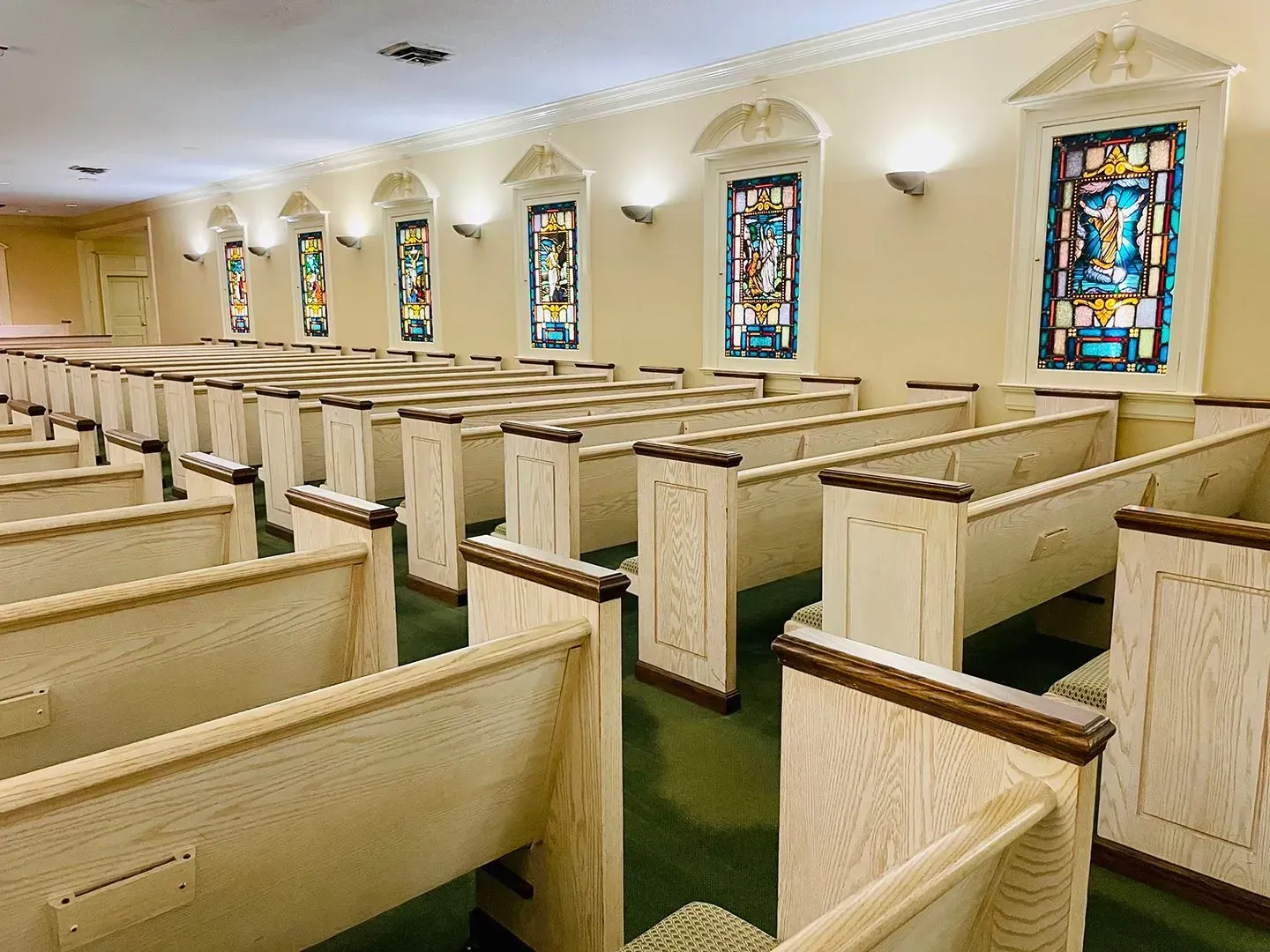 Empty church sanctuary with rows of wooden pews and stained-glass windows along the wall