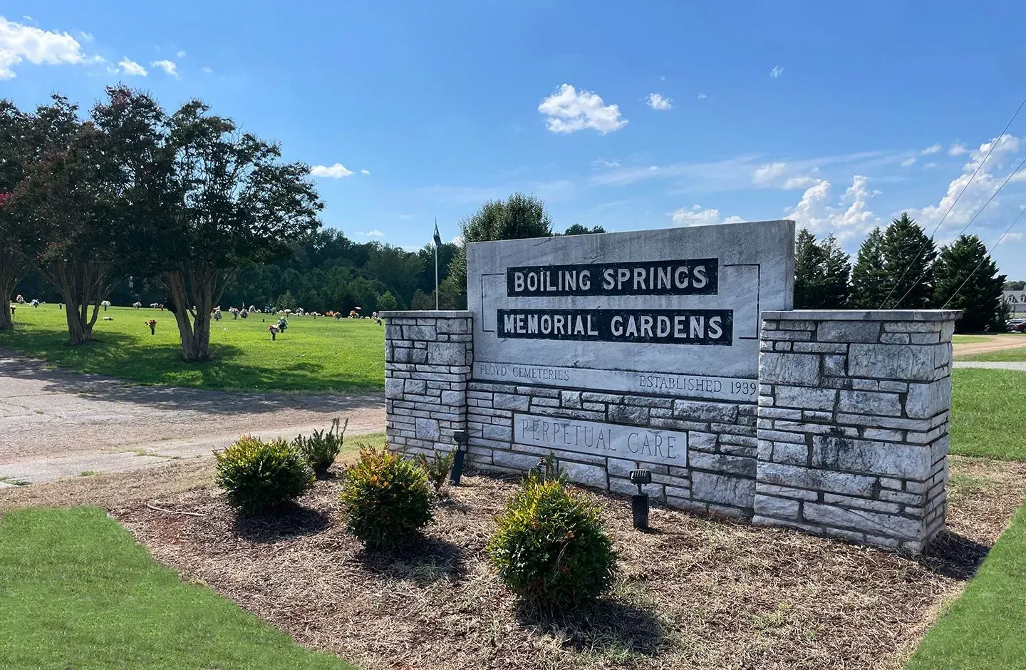 Boiling Springs Memorial Gardens stone sign beside a grassy path and trees under a blue sky