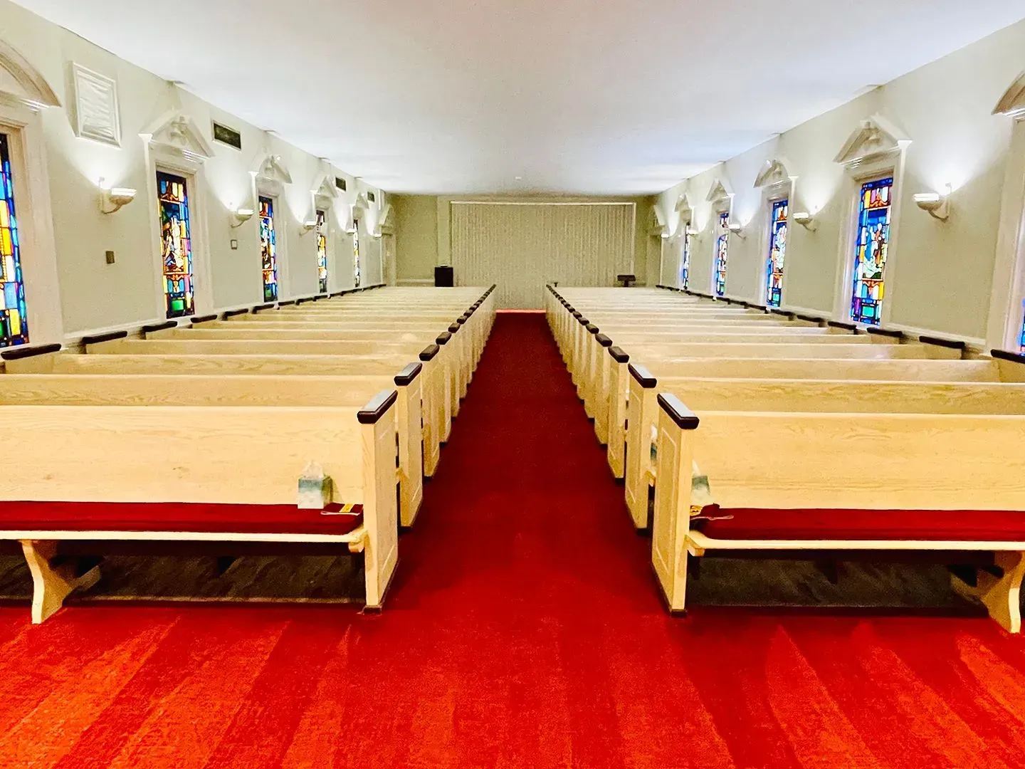 Empty church sanctuary with red carpet and rows of wooden pews facing the altar