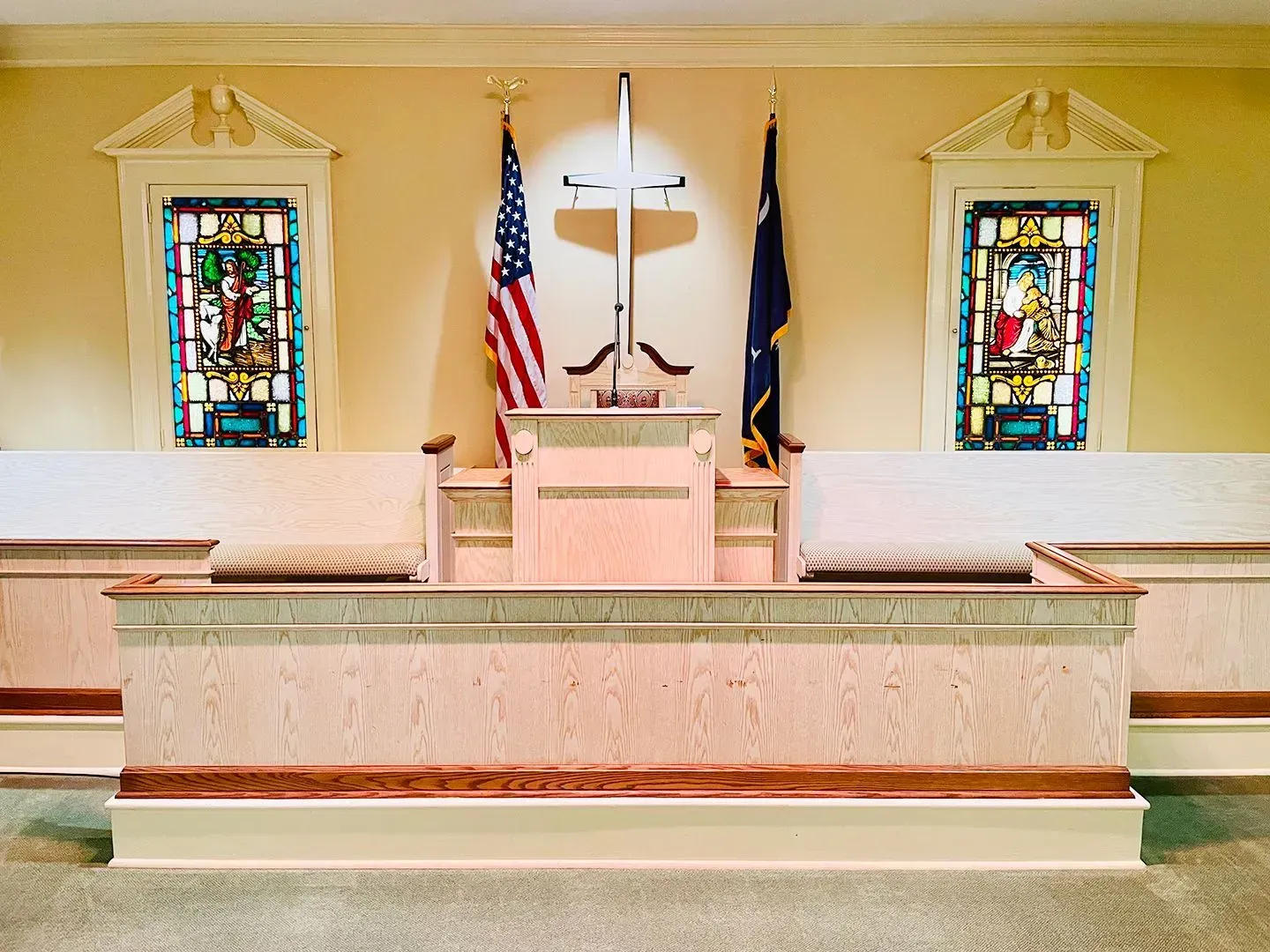 Church altar with cross, American flag, stained glass windows, and white pews on either side
