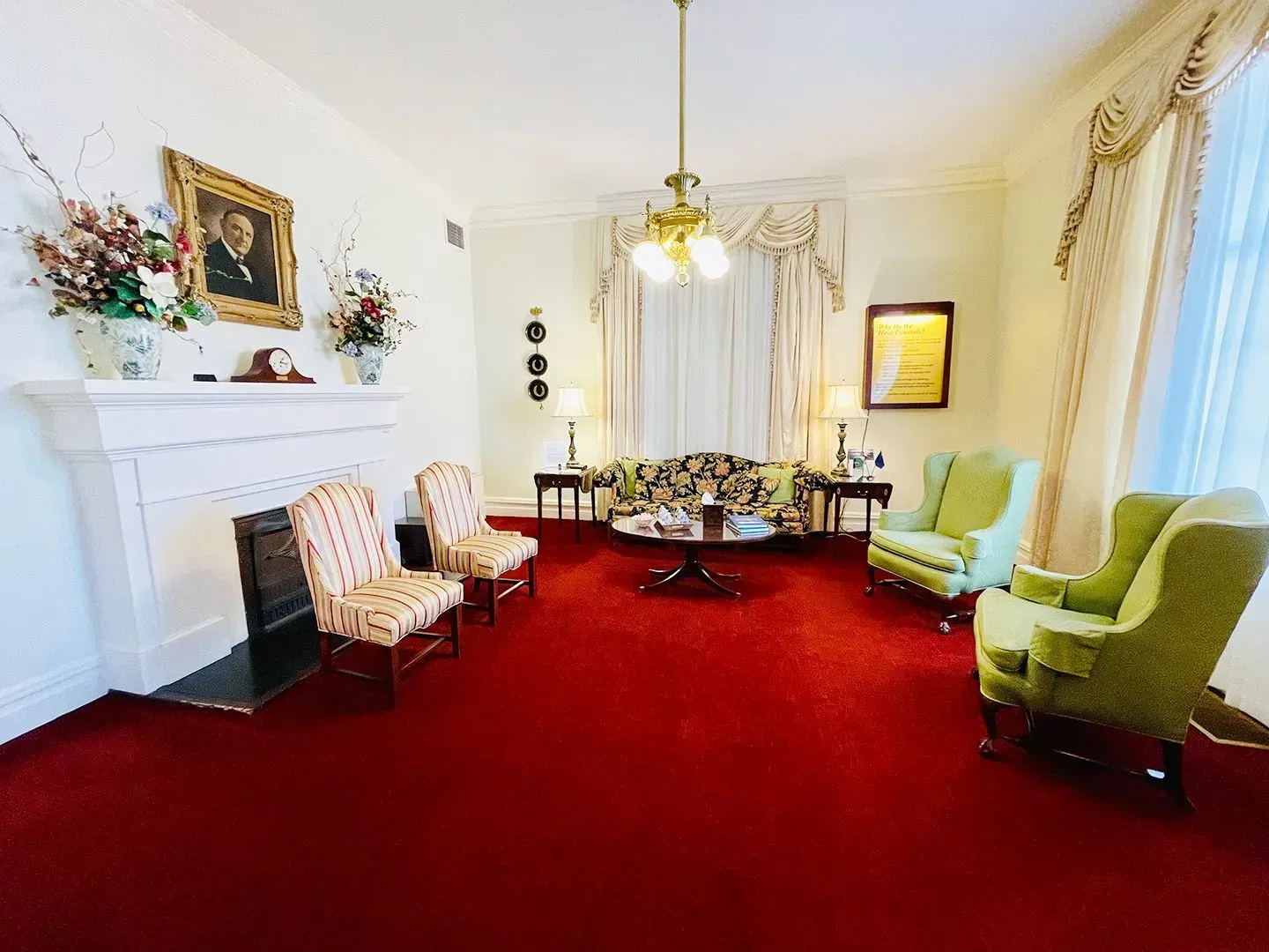 Elegant living room with red carpet, white fireplace, green armchairs, and a chandelier