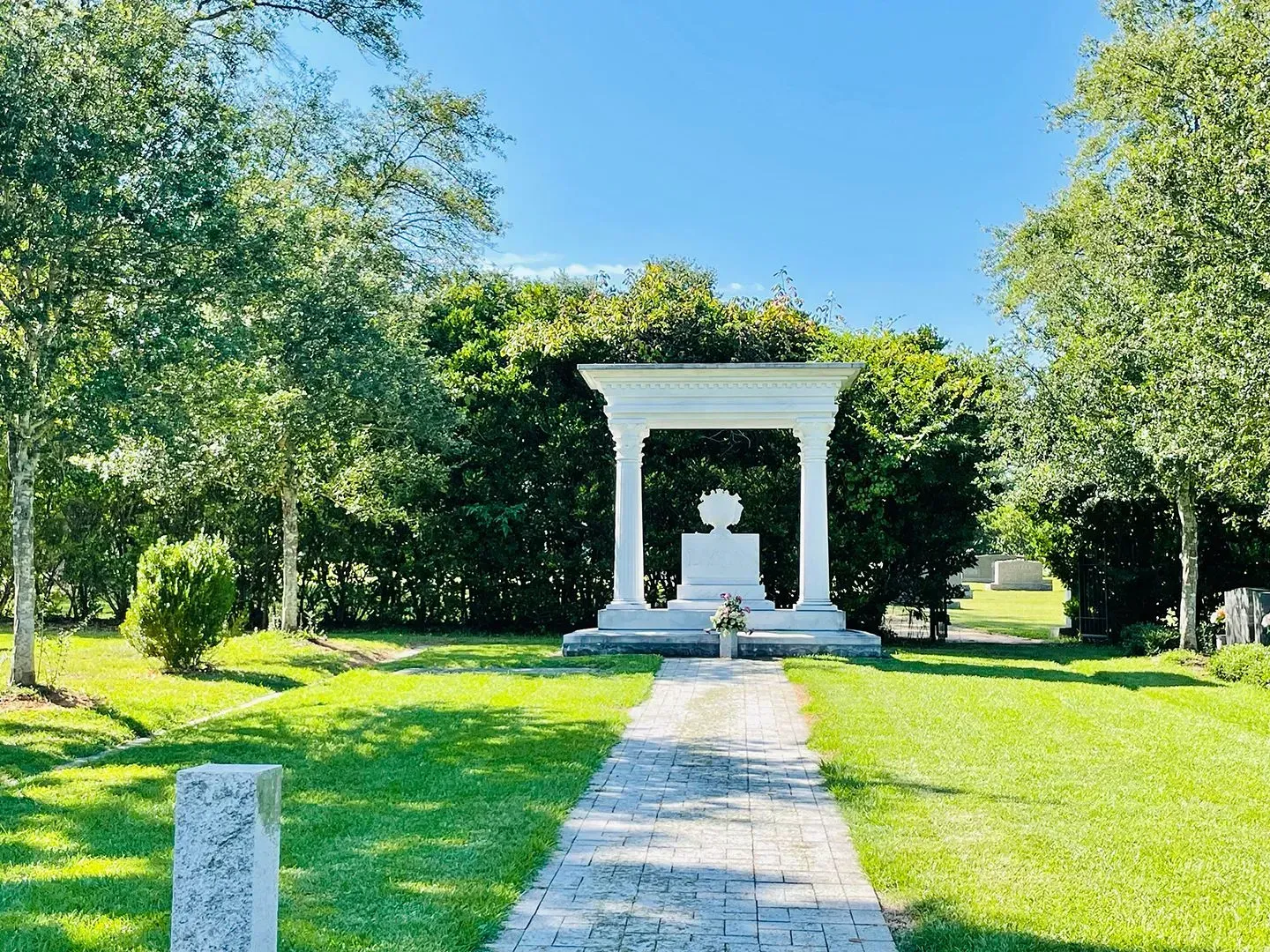 White garden archway at the end of a stone path in a sunny green park
