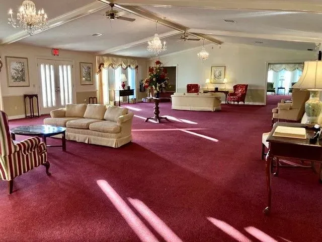 Spacious lounge with red carpet, beige sofas, tables, chandeliers, and a Christmas tree near the back wall