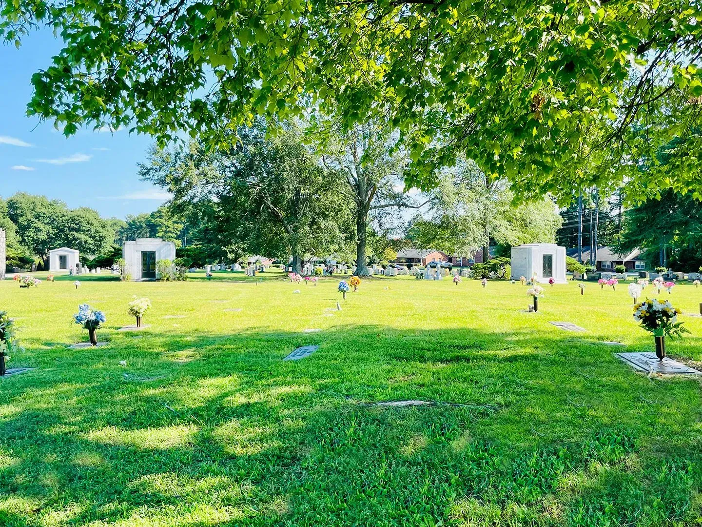Sunny cemetery lawn with small memorial markers and trees casting shade