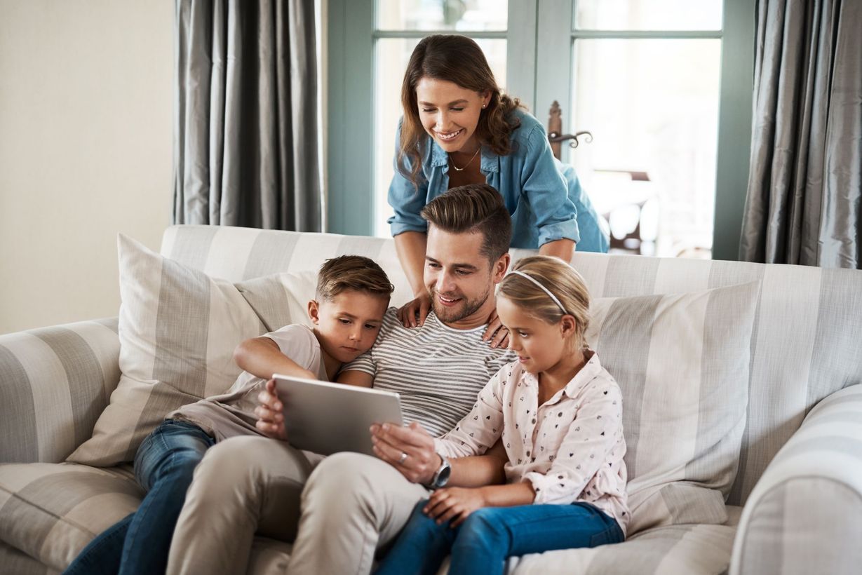 Family gathered on a couch, smiling and looking at a tablet in a bright living room