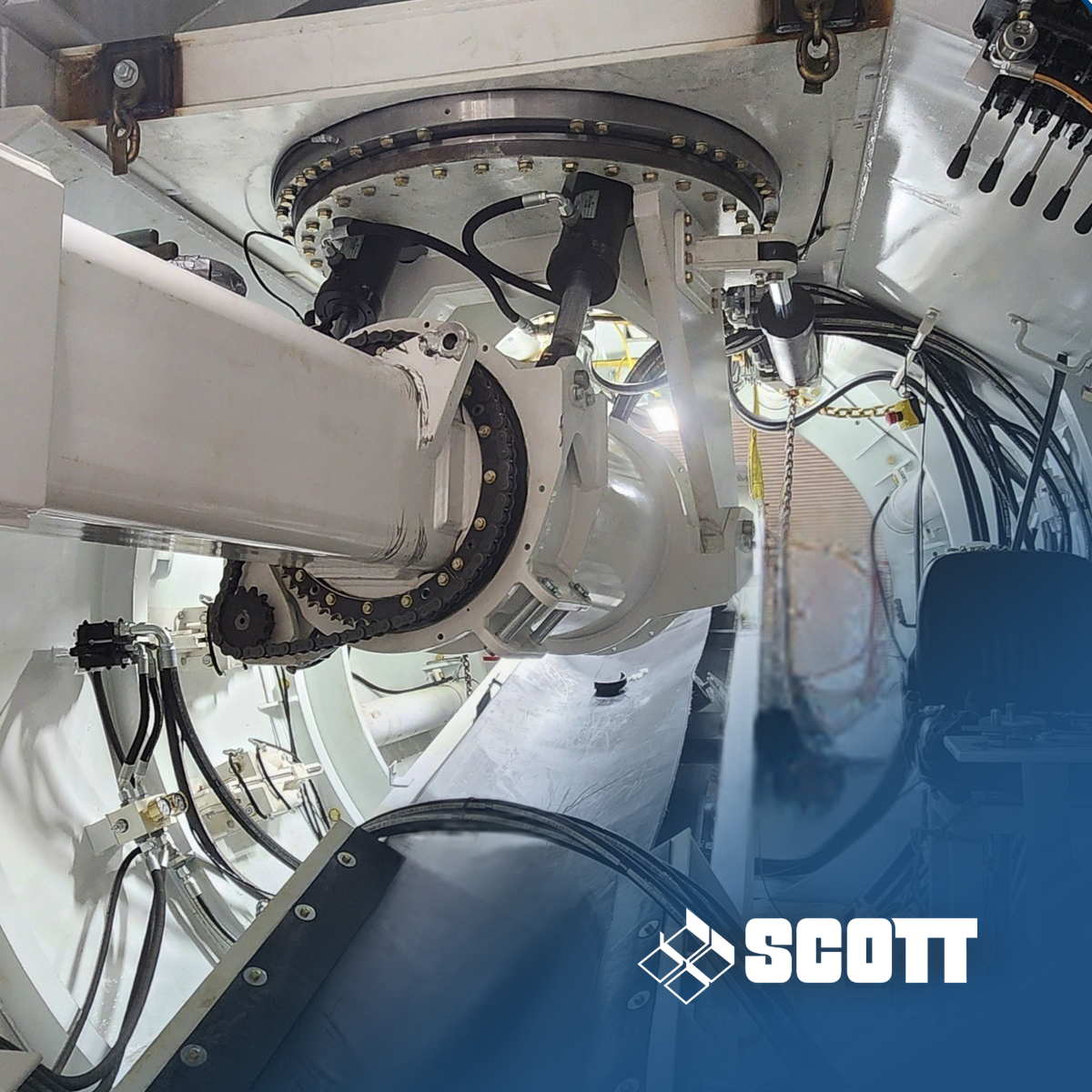 Inside a white metal interior, a person in a blue Scott jacket works among hoses and machinery.