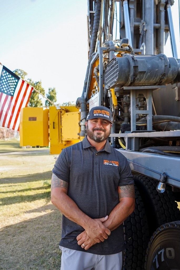 A man is standing in front of a truck with an american flag in the background.