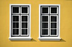 Two white-framed windows with black grid lines, on a yellow wall.
