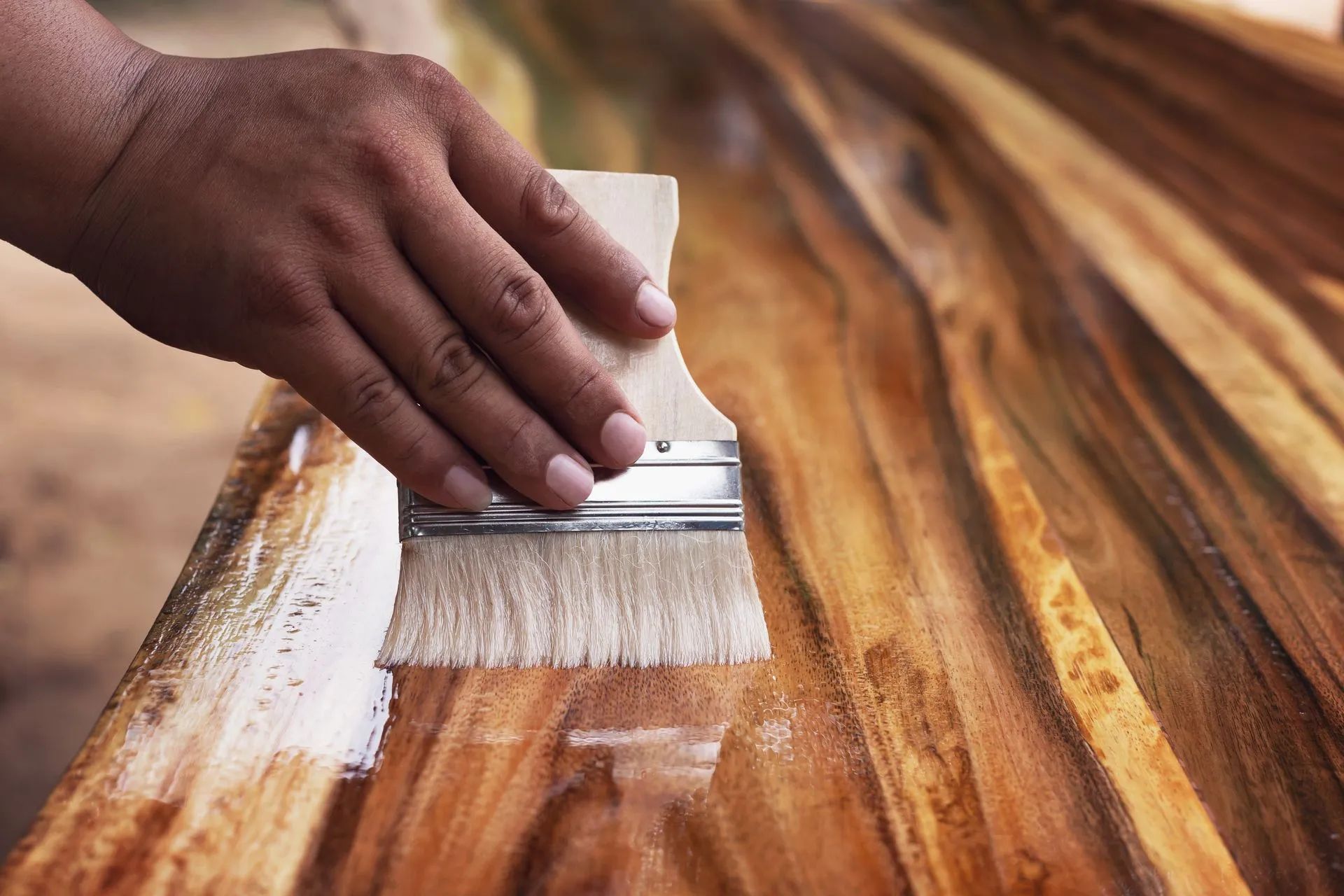 Person applying varnish to wooden surface with a brush.