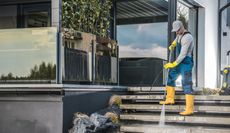 Man in yellow boots and gloves power washes steps of a modern building.
