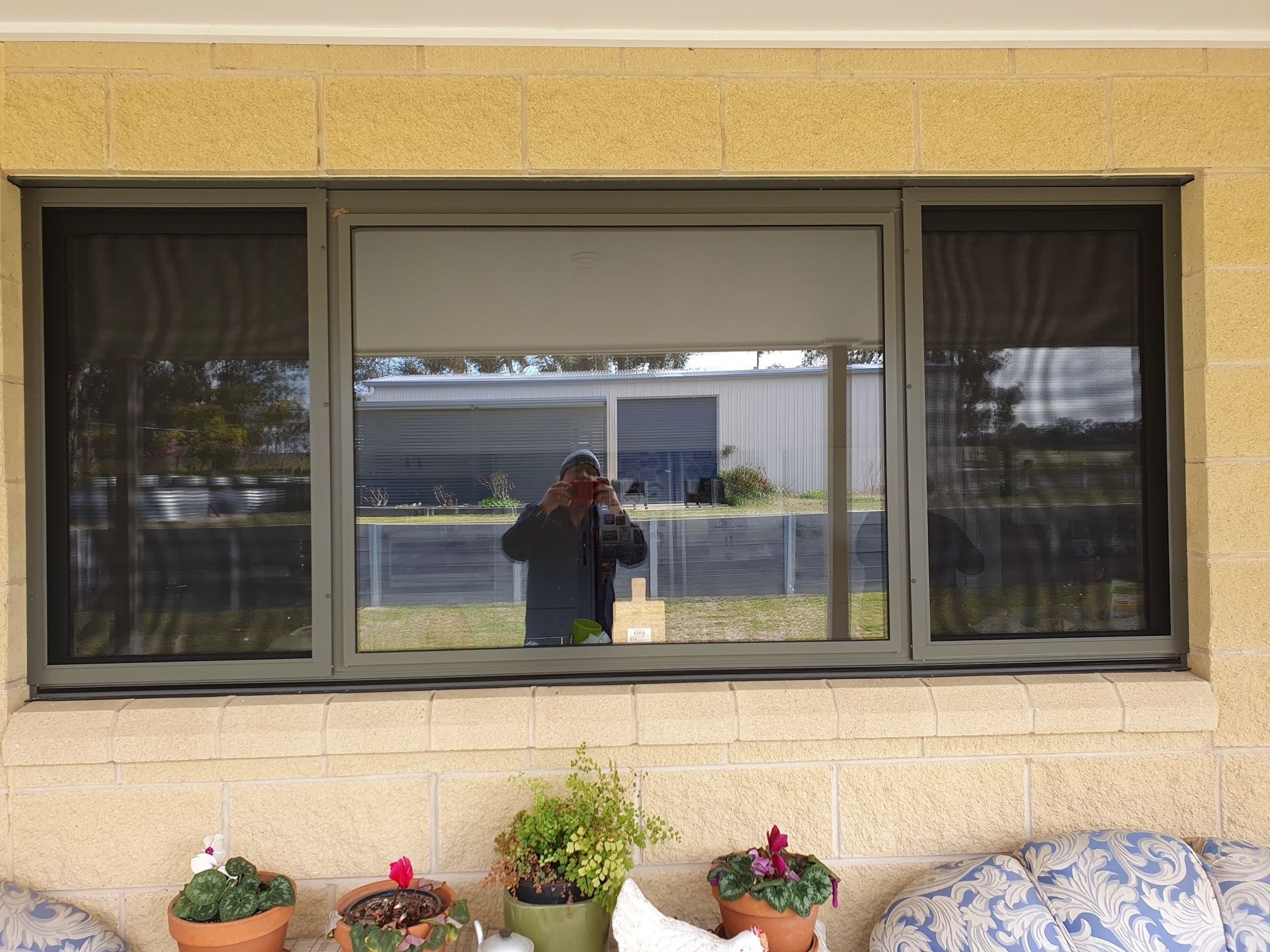 Window with center blind, side screens, reflecting person holding camera and outside view.