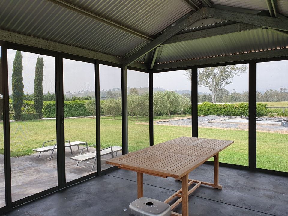 Enclosed outdoor dining area with screen walls and a large wooden table, overlooking a grassy lawn.