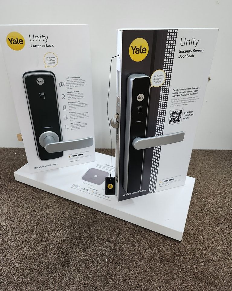 Two Yale Unity smart lock displays on a white shelf, showcasing the black locks with silver handles.
