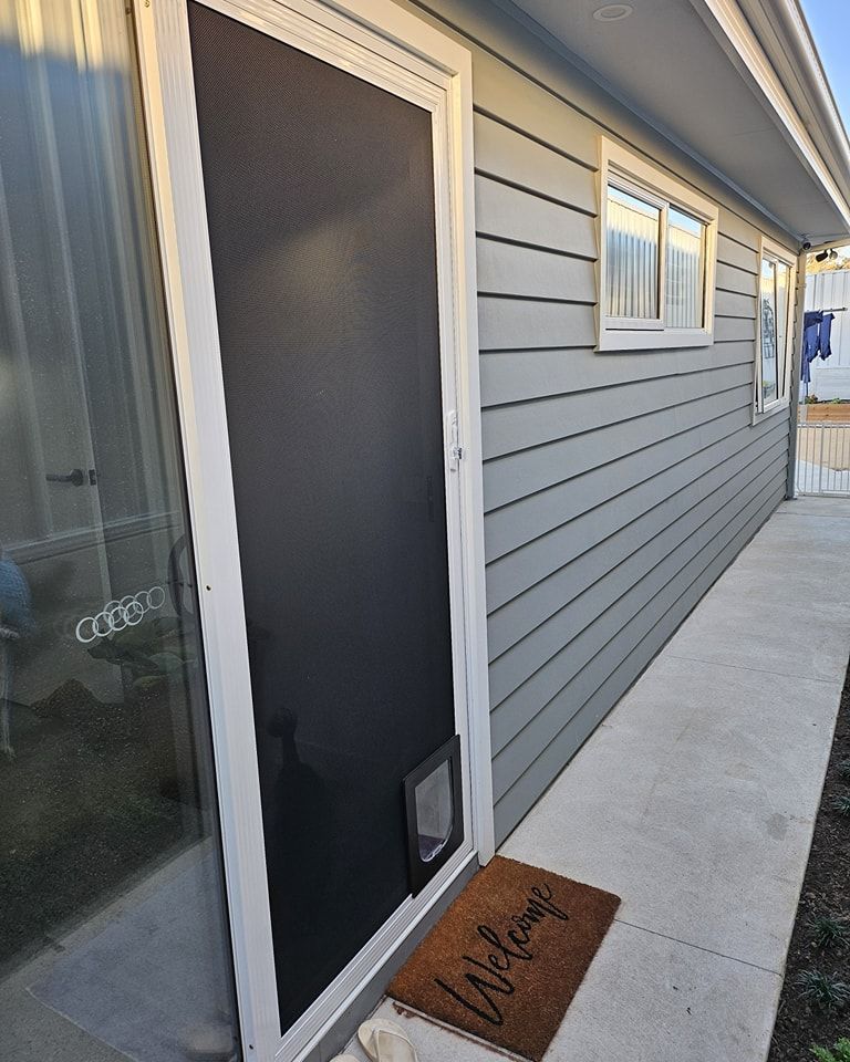 Screen door with cat flap, adjacent to a gray-sided house. 