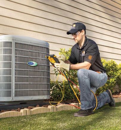 Technician kneels by outdoor air conditioner, using a gauge on the unit in a yard.