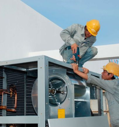 Two workers in hard hats repairing rooftop HVAC unit with tools