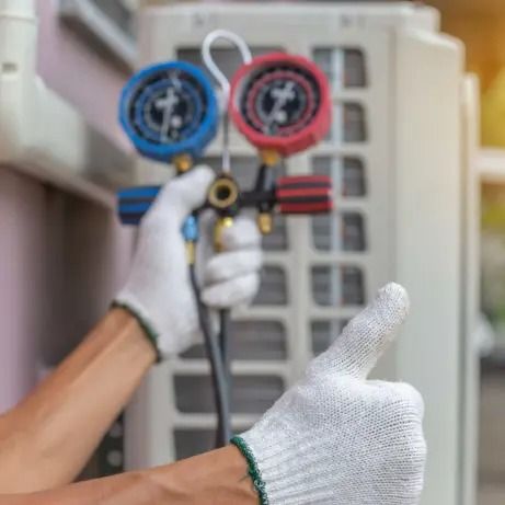 Gloved hands hold HVAC gauges near an outdoor AC unit, with a thumbs-up gesture.