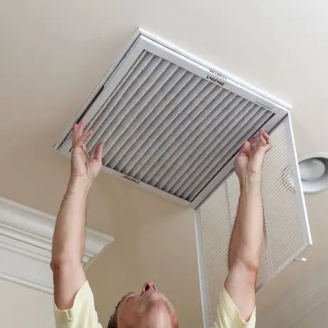 Person replacing a ceiling air filter, reaching up toward an open filter grille