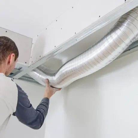 Worker installing silver HVAC duct in a ceiling space
