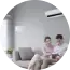 Two people sitting on a couch in a bright living room, viewing something on a laptop.