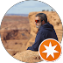 Woman in sunglasses looking out over a rocky desert landscape, with a circular orange logo in the corner