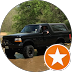 Black pickup truck parked on a road in front of green trees, with a white star badge overlay in the corner