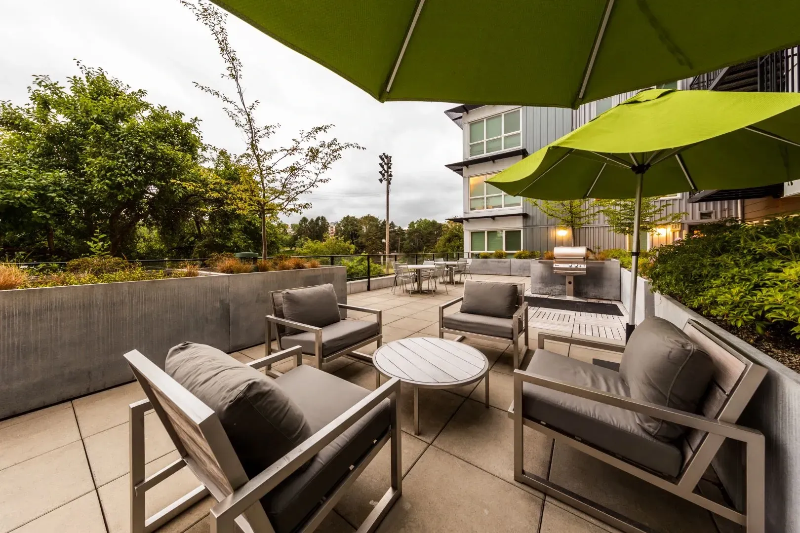 Modern outdoor seating area with chairs, table, and umbrella next to a grill and building.